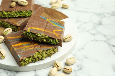 Photo of Pieces of Dubai chocolate bar and pistachios on white marble table, closeup