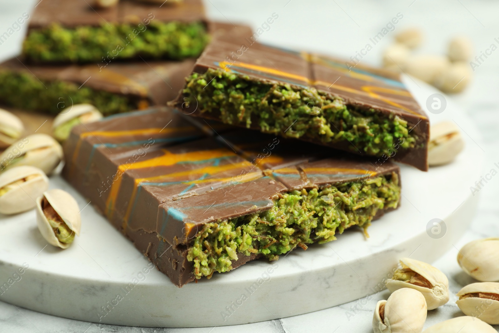 Photo of Pieces of Dubai chocolate bar and pistachios on white table, closeup