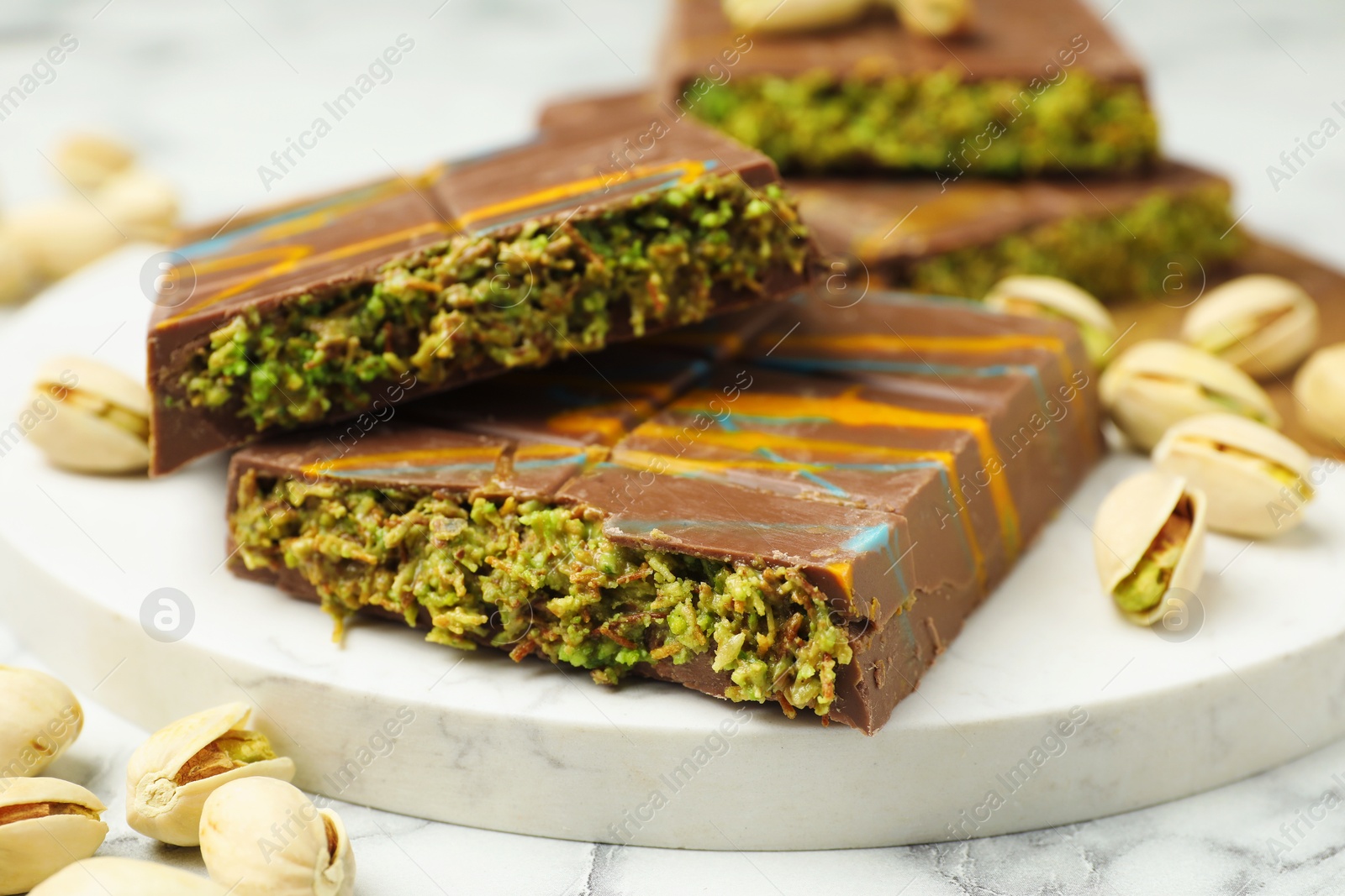 Photo of Pieces of Dubai chocolate bar and pistachios on white marble table, closeup