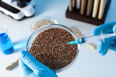 Photo of GMO concept. Scientist injecting something into buckwheat grains at table in laboratory, above view