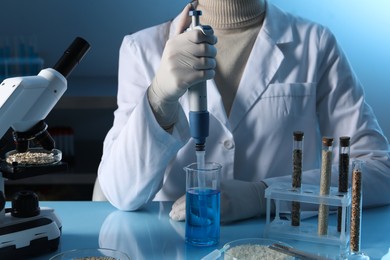 Photo of GMO concept. Scientist dripping sample into beaker at table with test tubes of cereal grains in laboratory, closeup