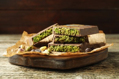 Photo of Pieces of Dubai chocolate bar with pistachios, knafeh and cacao chips on wooden table, closeup