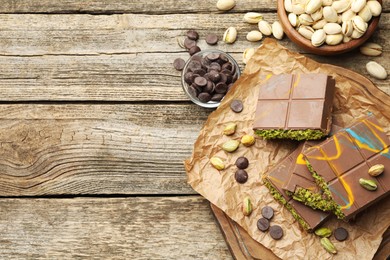 Photo of Pieces of Dubai chocolate bars with pistachios, knafeh and cacao chips on wooden table, flat lay. Space for text