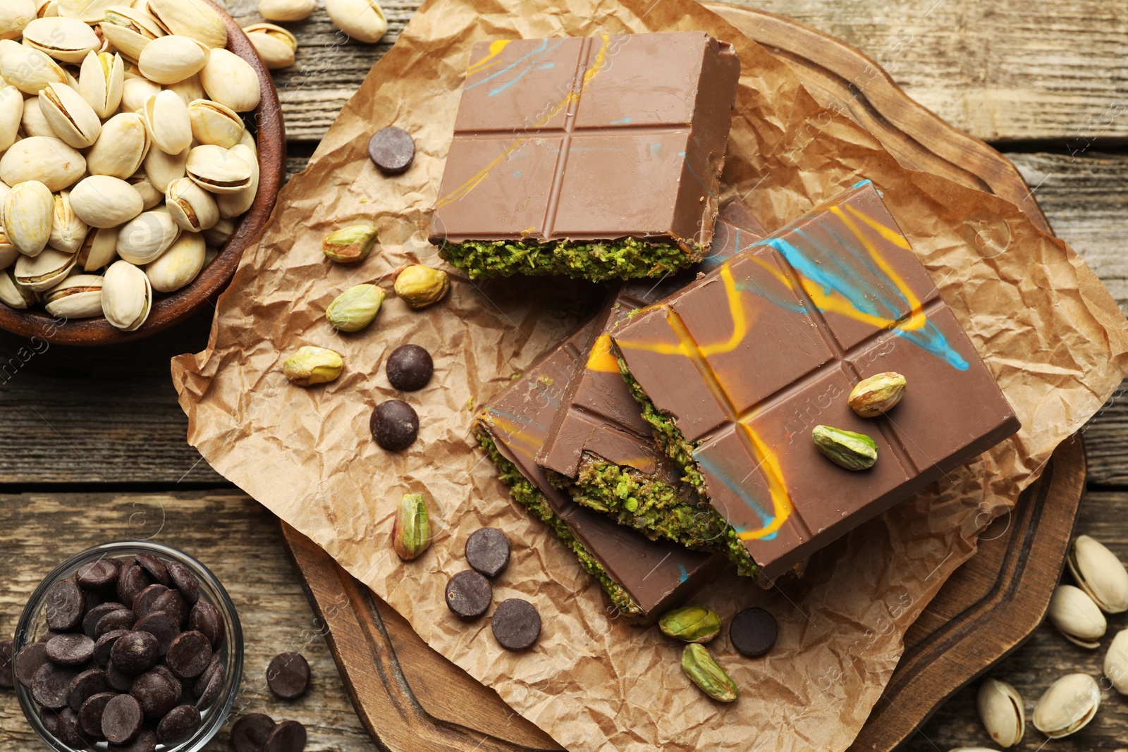 Photo of Pieces of Dubai chocolate bars with pistachios, knafeh and cacao chips on wooden table, flat lay