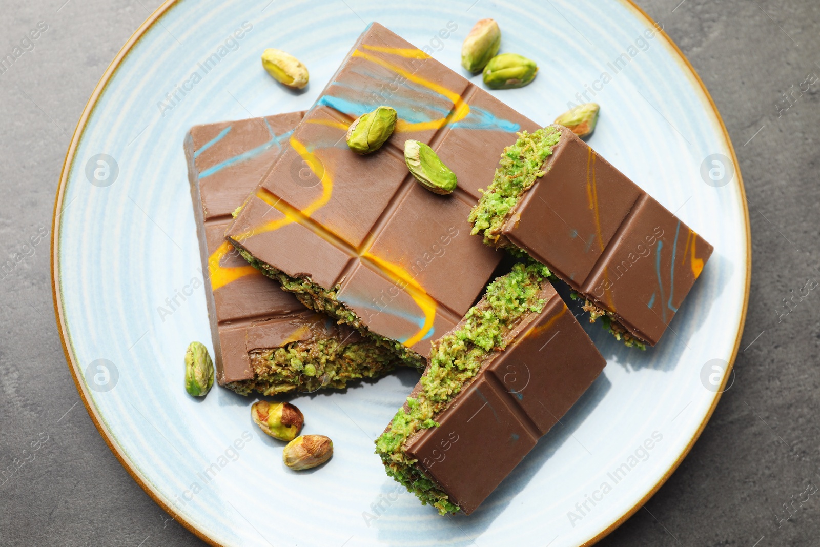 Photo of Pieces of Dubai chocolate bar with pistachios and knafeh on grey table, top view