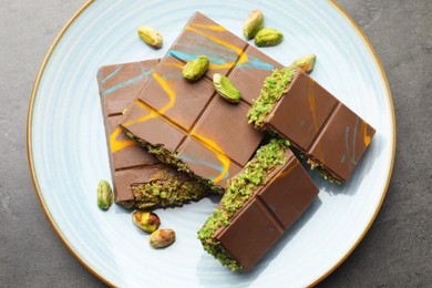 Photo of Pieces of Dubai chocolate bar with pistachios and knafeh on grey table, top view