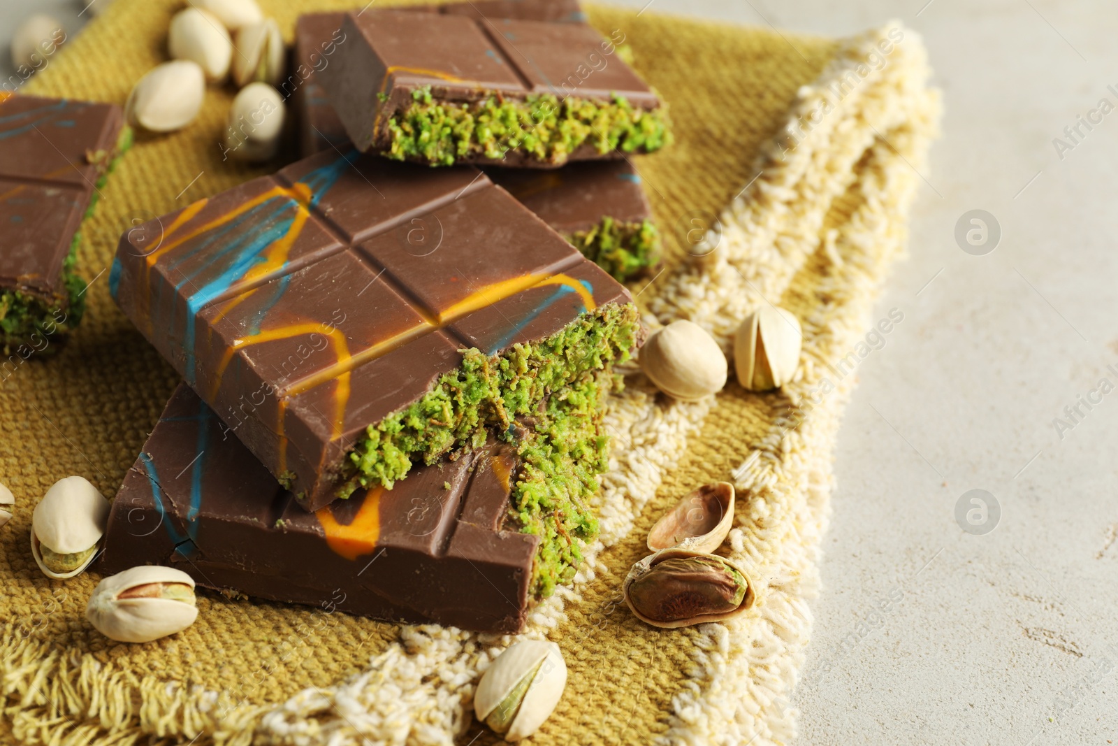 Photo of Pieces of Dubai chocolate bar with pistachios and knafeh on light table, closeup