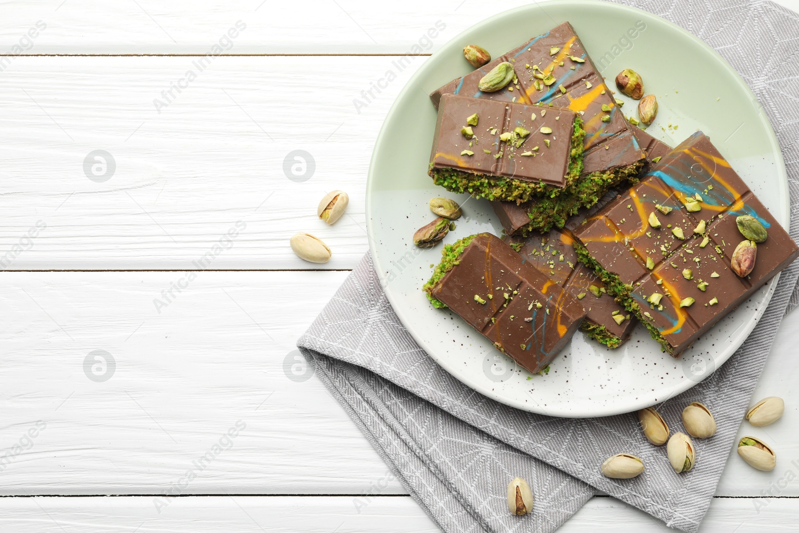 Photo of Pieces of Dubai chocolate bars with pistachios and knafeh on white wooden table, flat lay. Space for text