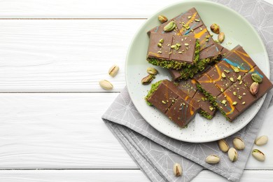 Photo of Pieces of Dubai chocolate bars with pistachios and knafeh on white wooden table, flat lay. Space for text