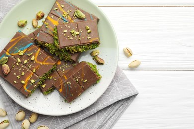 Photo of Pieces of Dubai chocolate bars with pistachios and knafeh on white wooden table, flat lay. Space for text