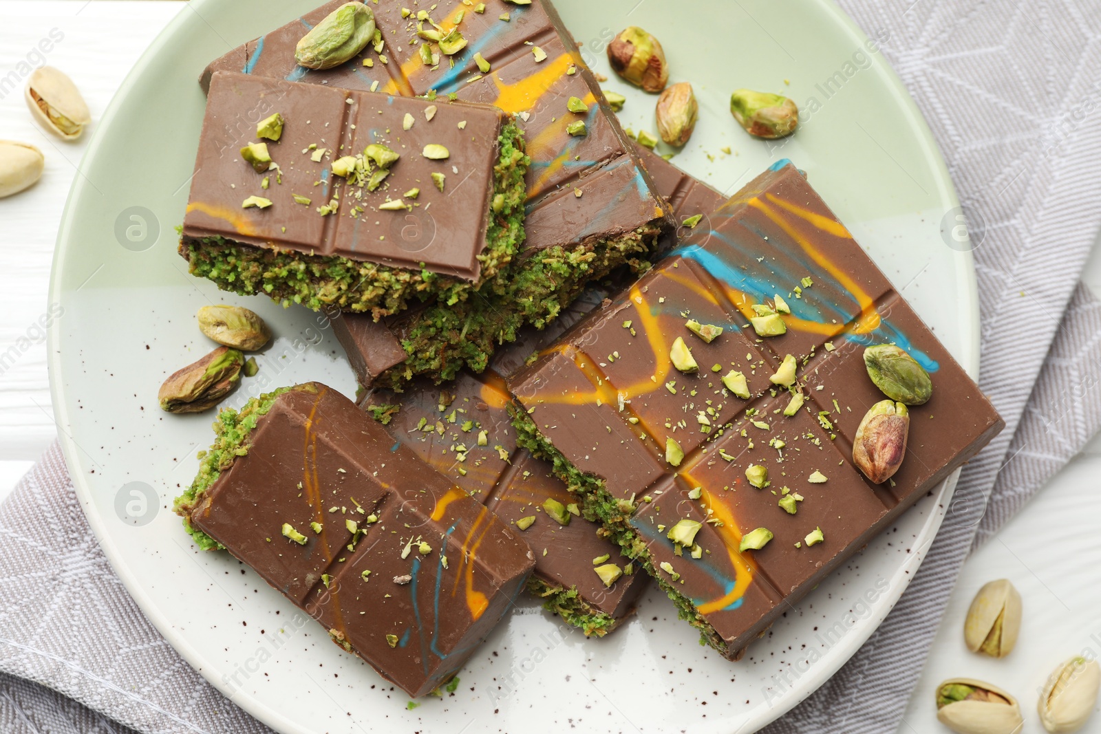 Photo of Pieces of Dubai chocolate bars with pistachios and knafeh on white wooden table, flat lay