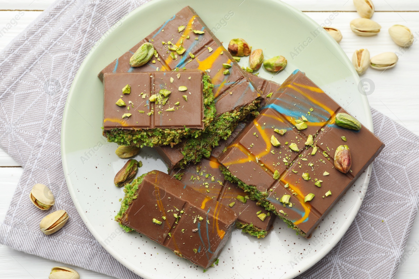 Photo of Pieces of Dubai chocolate bars with pistachios and knafeh on white wooden table, flat lay