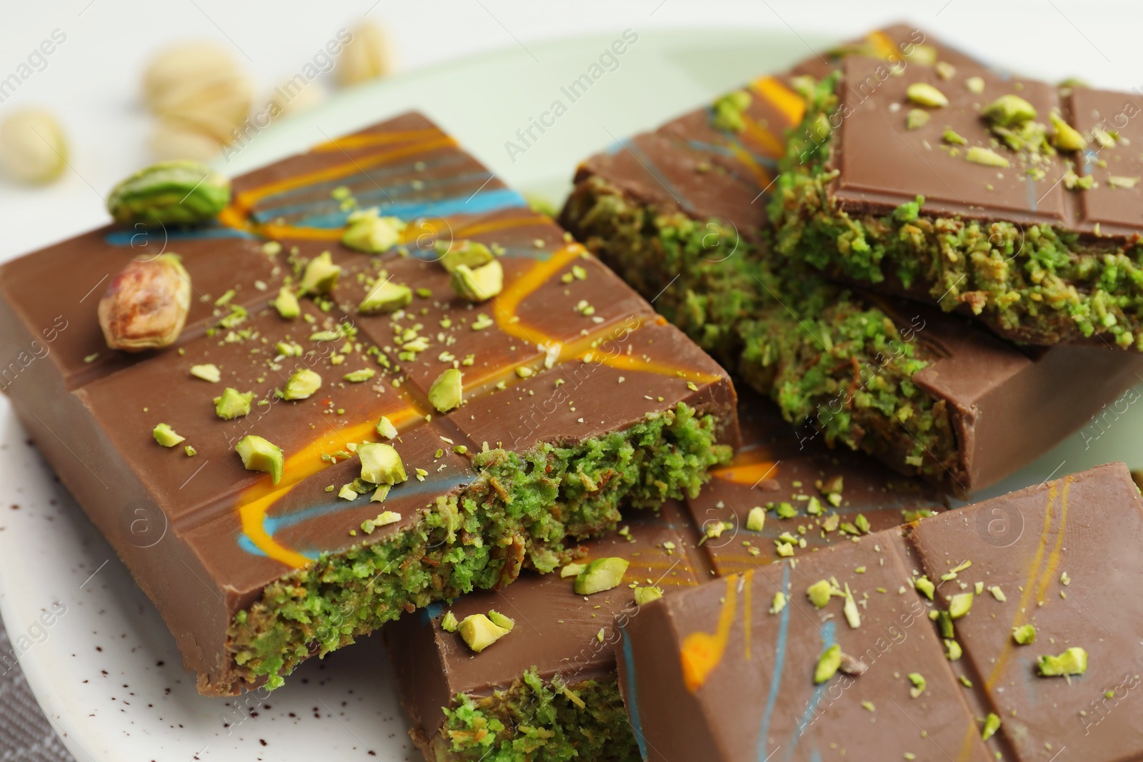 Photo of Pieces of Dubai chocolate bar with pistachio and knafeh on white table, closeup