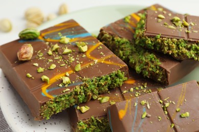 Photo of Pieces of Dubai chocolate bar with pistachio and knafeh on white table, closeup