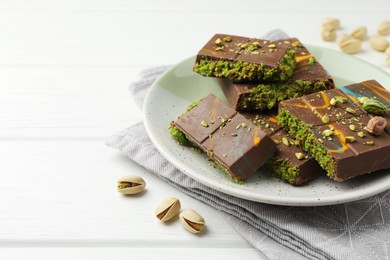 Photo of Pieces of Dubai chocolate bars with pistachios and knafeh on white wooden table, closeup. Space for text