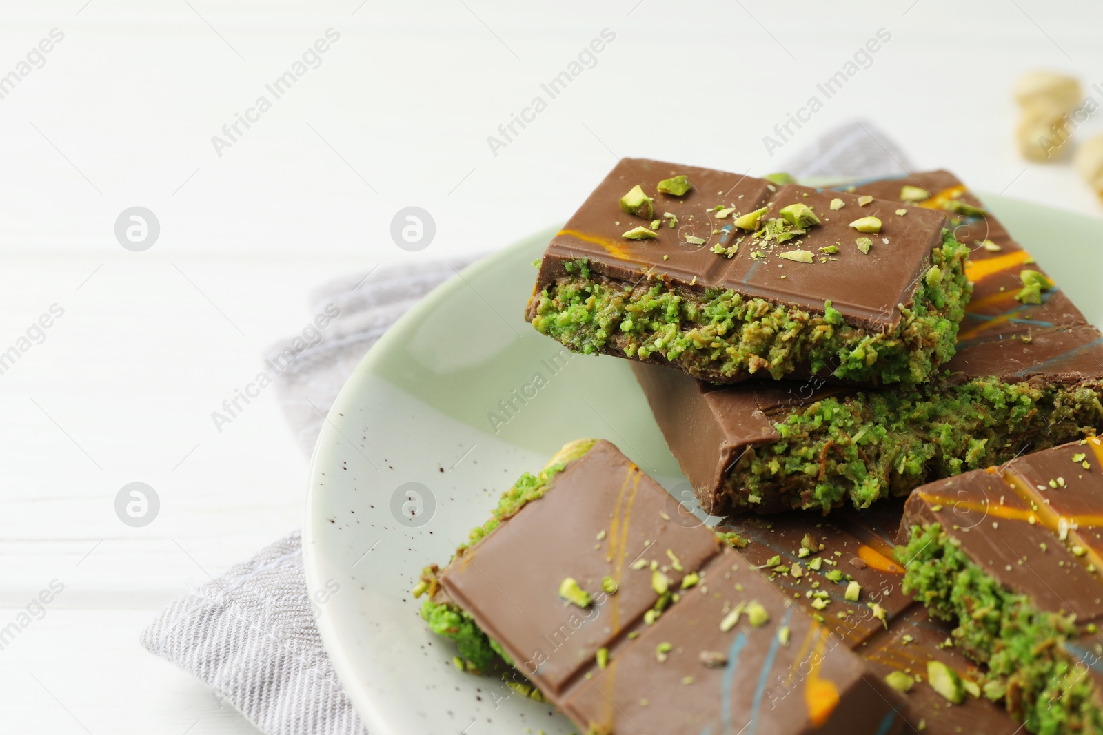 Photo of Pieces of Dubai chocolate bars with pistachio and knafeh on white wooden table, closeup. Space for text