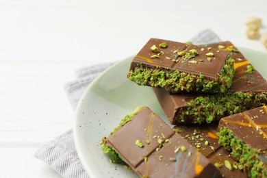 Photo of Pieces of Dubai chocolate bars with pistachio and knafeh on white wooden table, closeup. Space for text