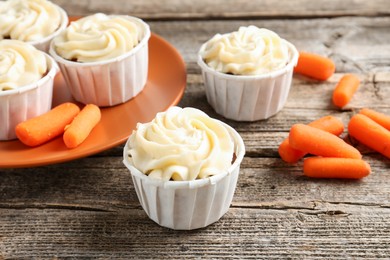 Photo of Delicious carrot muffins and fresh vegetables on wooden table, closeup