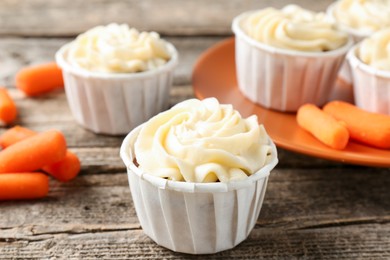 Photo of Delicious carrot muffins and fresh vegetables on wooden table, closeup