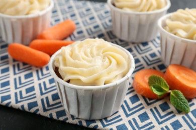 Photo of Delicious carrot muffins with fresh vegetables on black table, closeup