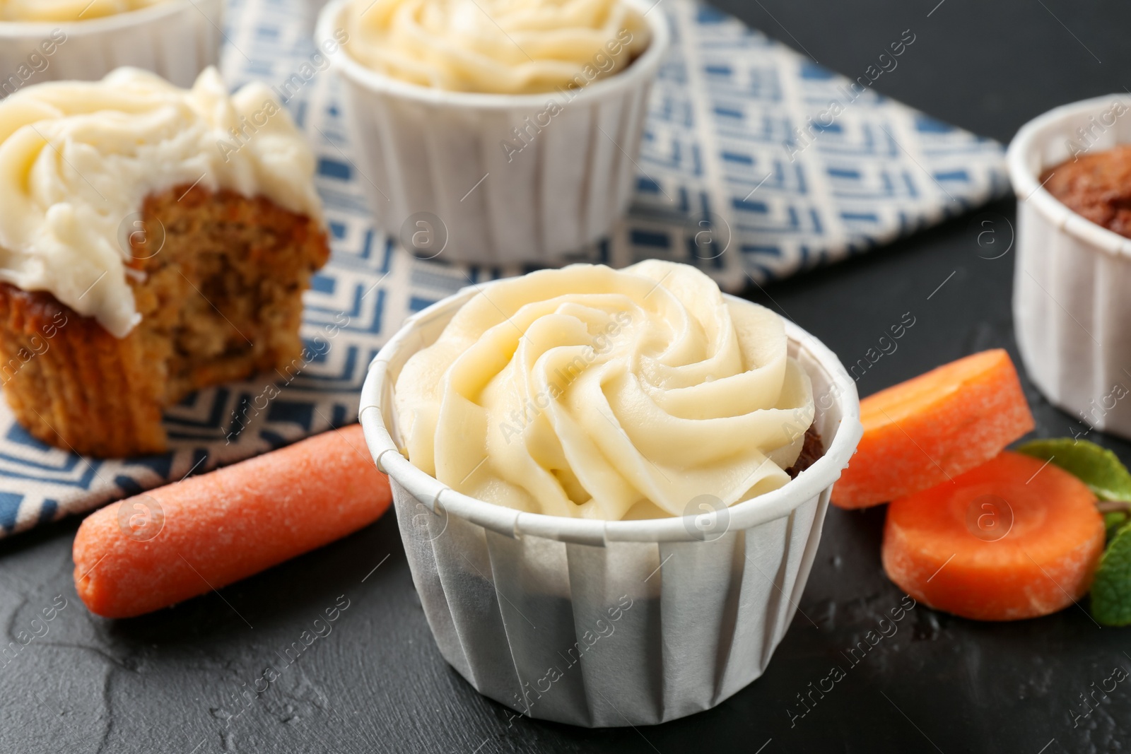 Photo of Delicious carrot muffins with fresh vegetables on black table, closeup