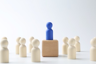 Photo of Human figures around wooden block with blue figure on top against white background. Competition concept