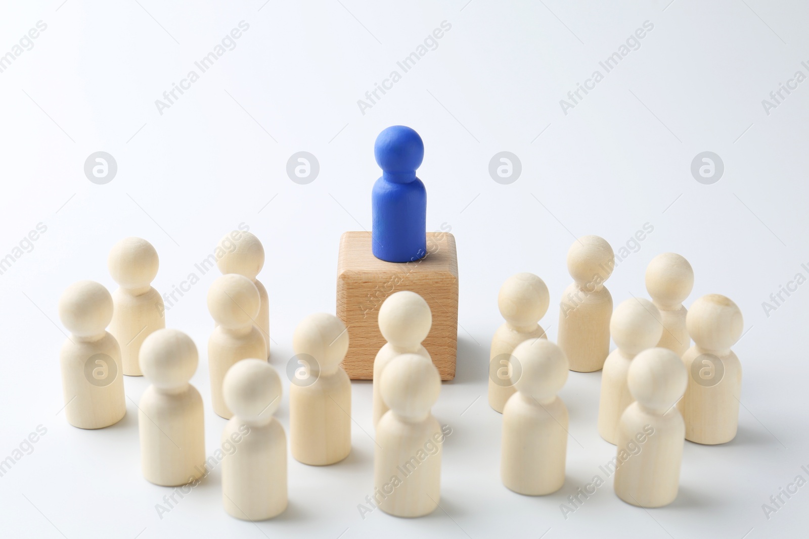 Photo of Human figures around wooden block with blue figure on top against white background. Competition concept