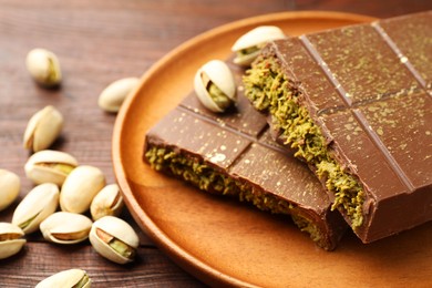 Photo of Pieces of tasty Dubai chocolate with pistachios and knafeh on wooden table, closeup