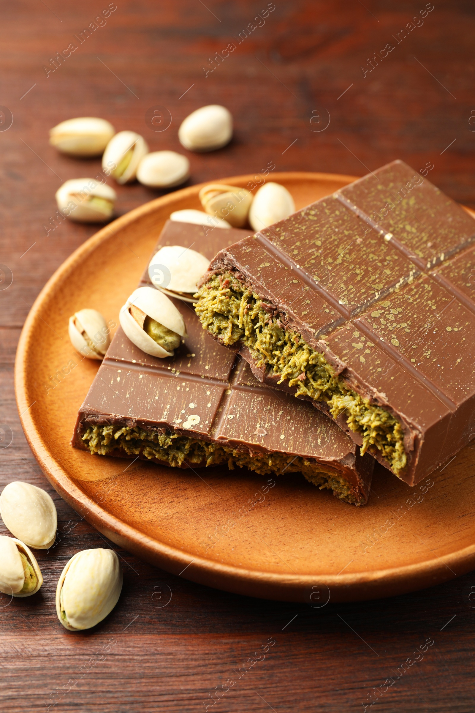 Photo of Pieces of tasty Dubai chocolate with pistachios and knafeh on wooden table, closeup