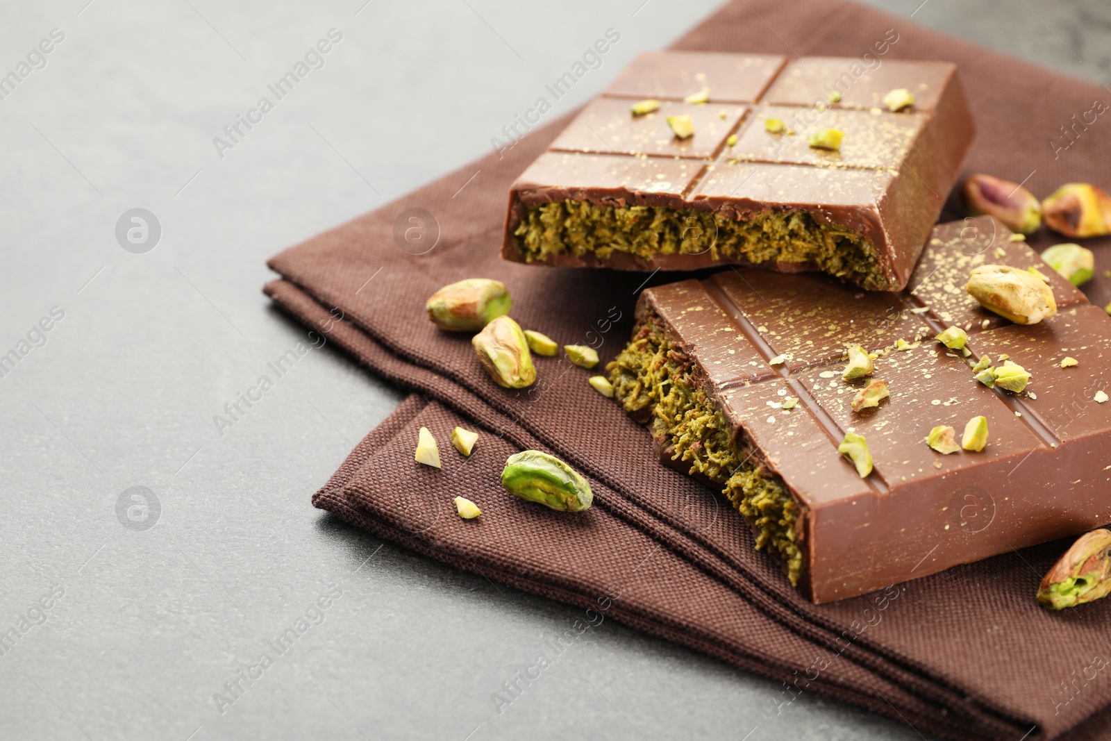 Photo of Pieces of tasty Dubai chocolate with pistachios and knafeh on grey table, closeup. Space for text