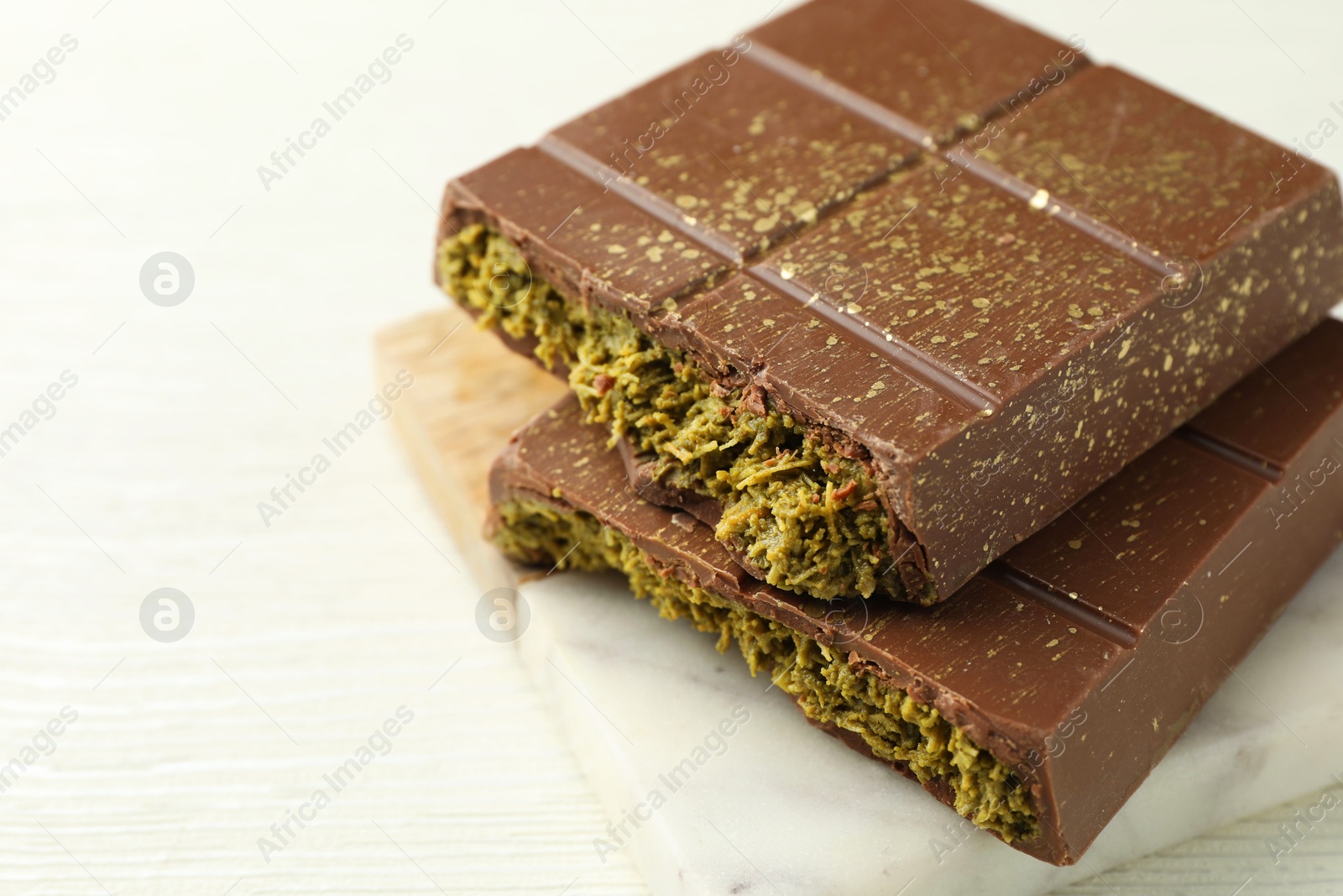 Photo of Pieces of tasty Dubai chocolate with pistachios and knafeh on white wooden table, closeup. Space for text