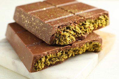 Photo of Pieces of tasty Dubai chocolate with pistachios and knafeh on white wooden table, closeup