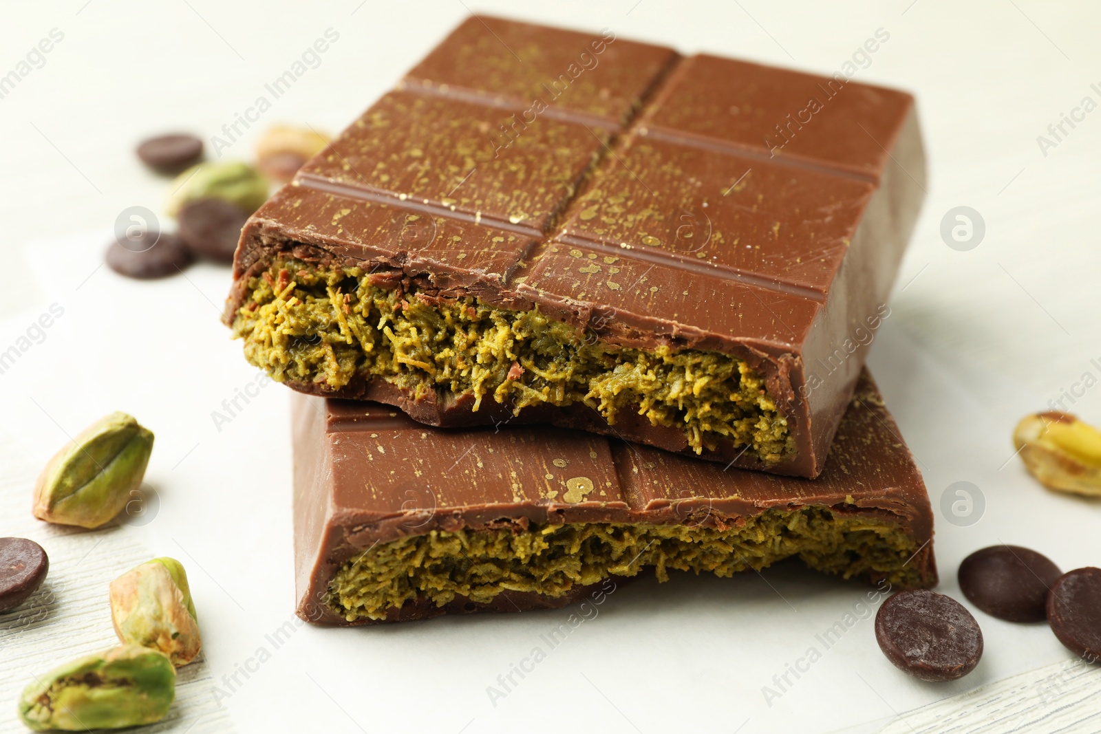 Photo of Pieces of tasty Dubai chocolate with pistachios, knafeh and cacao chips on white wooden table, closeup