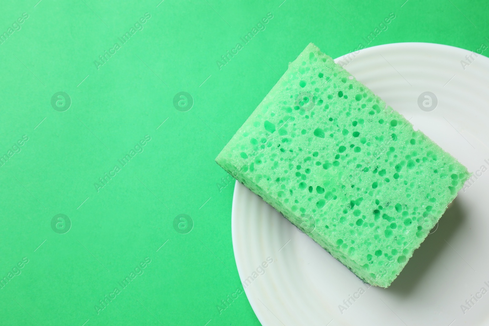 Photo of Plate with sponge on green background, top view. Space for text