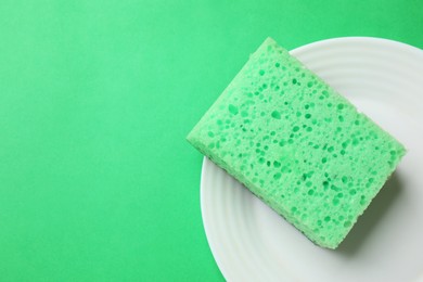 Photo of Plate with sponge on green background, top view. Space for text