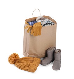 Photo of Used clothes in paper bag, hat and boots isolated on white