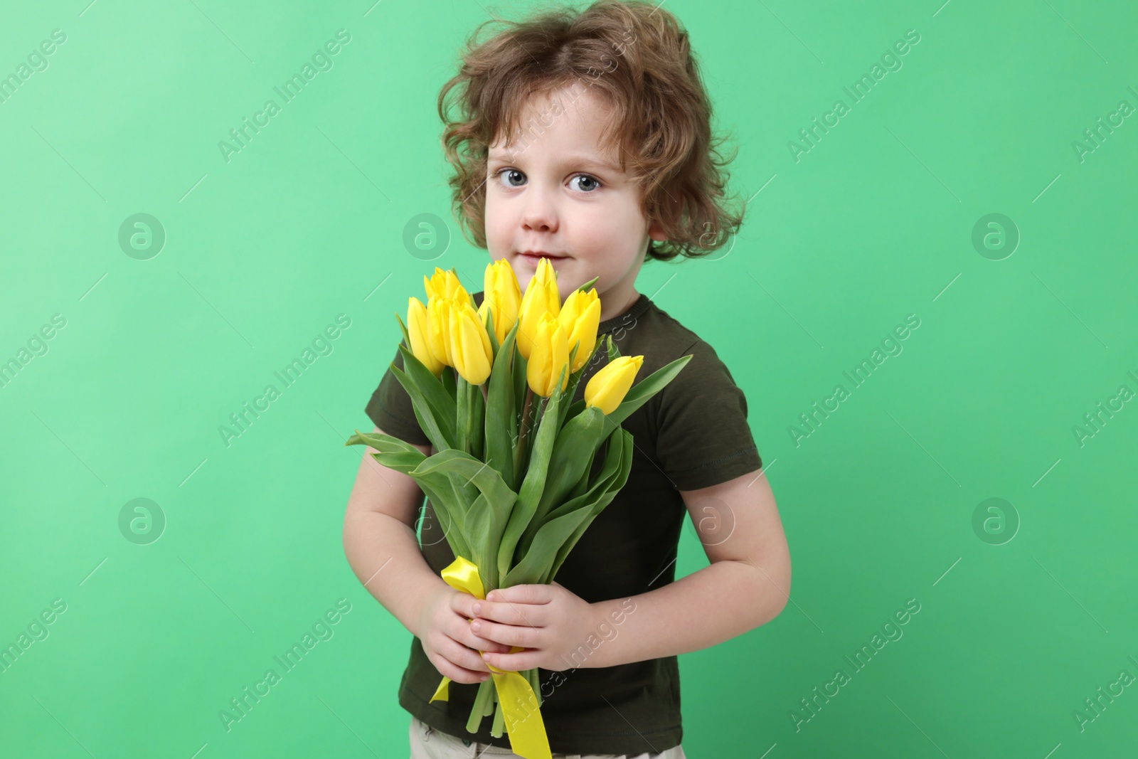 Photo of Cute little boy with bouquet of tulips on green background