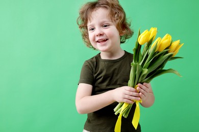 Photo of Cute little boy with bouquet of tulips on green background. Space for text