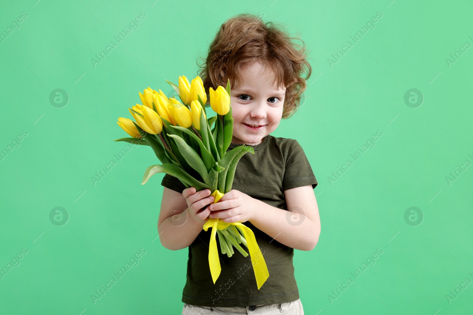 Photo of Cute little boy with bouquet of tulips on green background