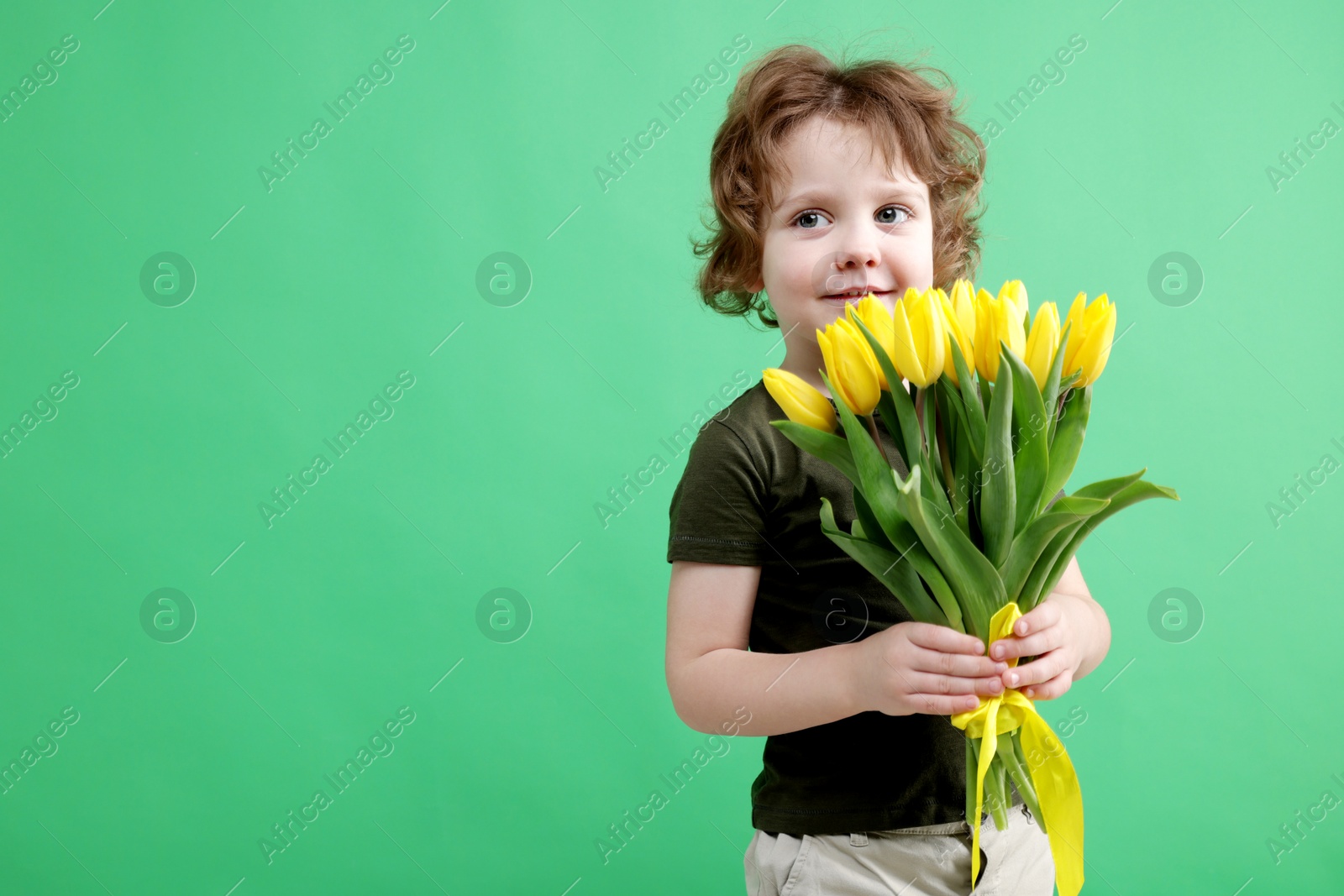 Photo of Cute little boy with bouquet of tulips on green background. Space for text