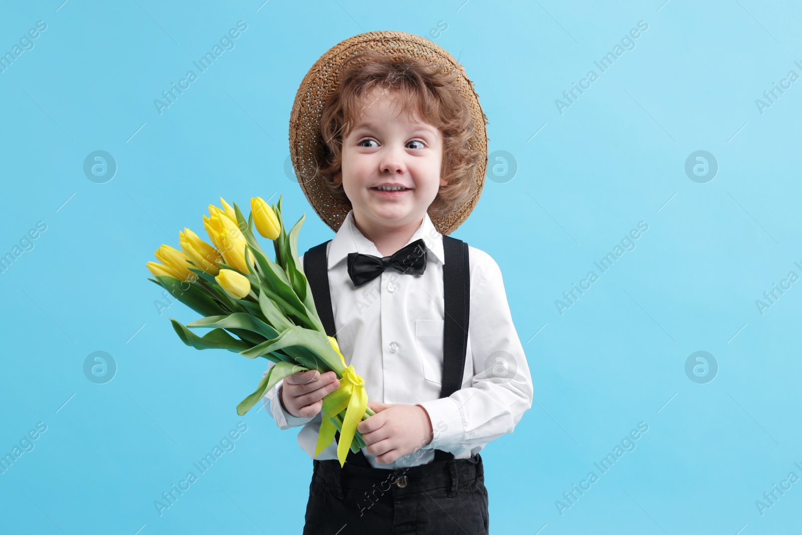 Photo of Cute little boy in wicker hat with bouquet of tulips on light blue background