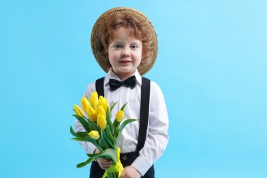 Photo of Cute little boy in wicker hat with bouquet of tulips on light blue background