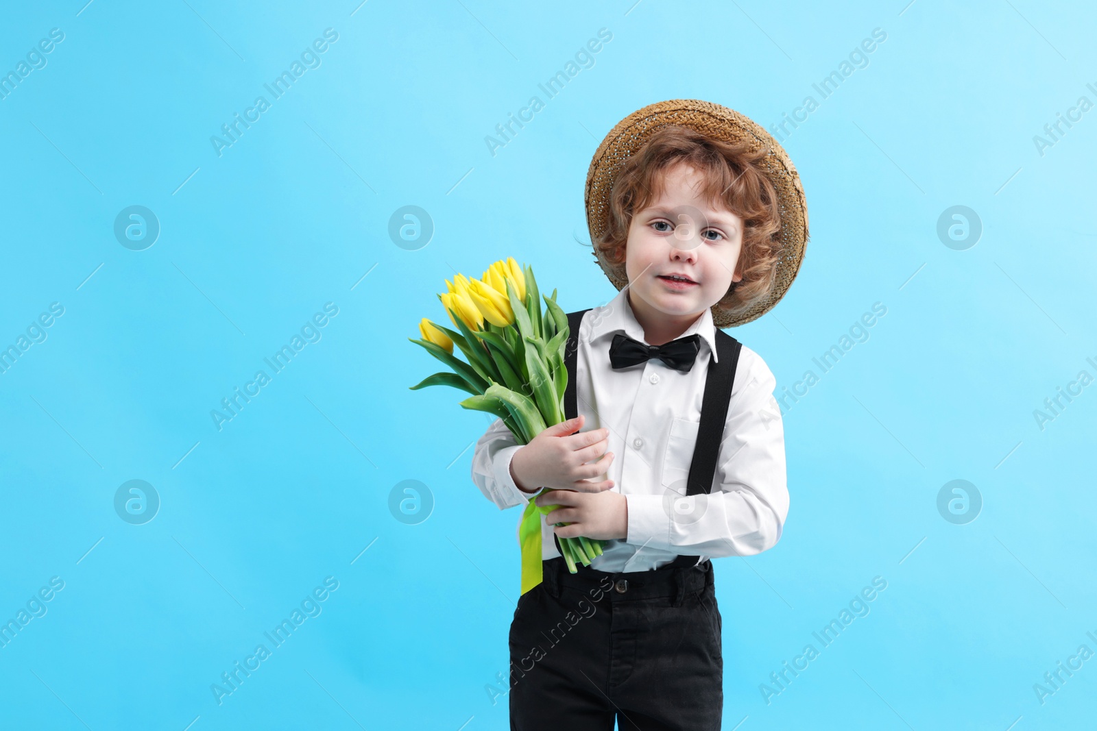 Photo of Cute little boy in wicker hat with bouquet of tulips on light blue background. Space for text