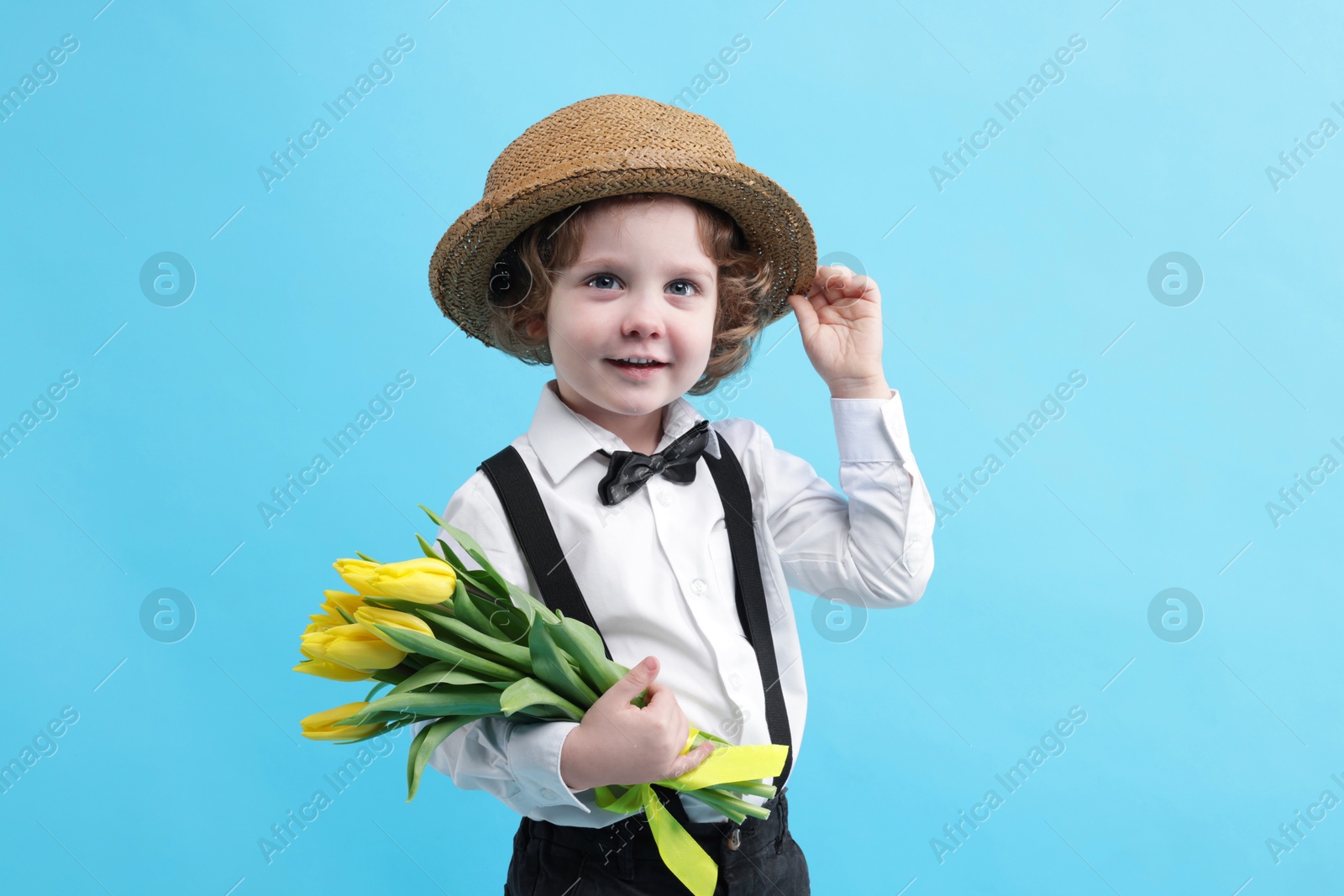 Photo of Cute little boy in wicker hat with bouquet of tulips on light blue background