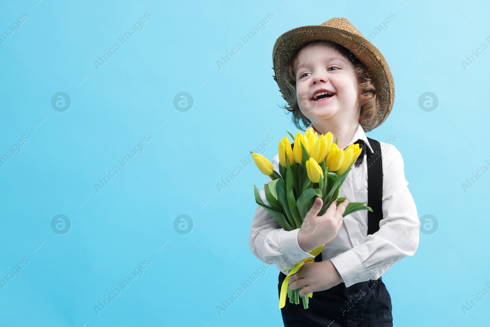 Photo of Cute little boy in wicker hat with bouquet of tulips on light blue background. Space for text