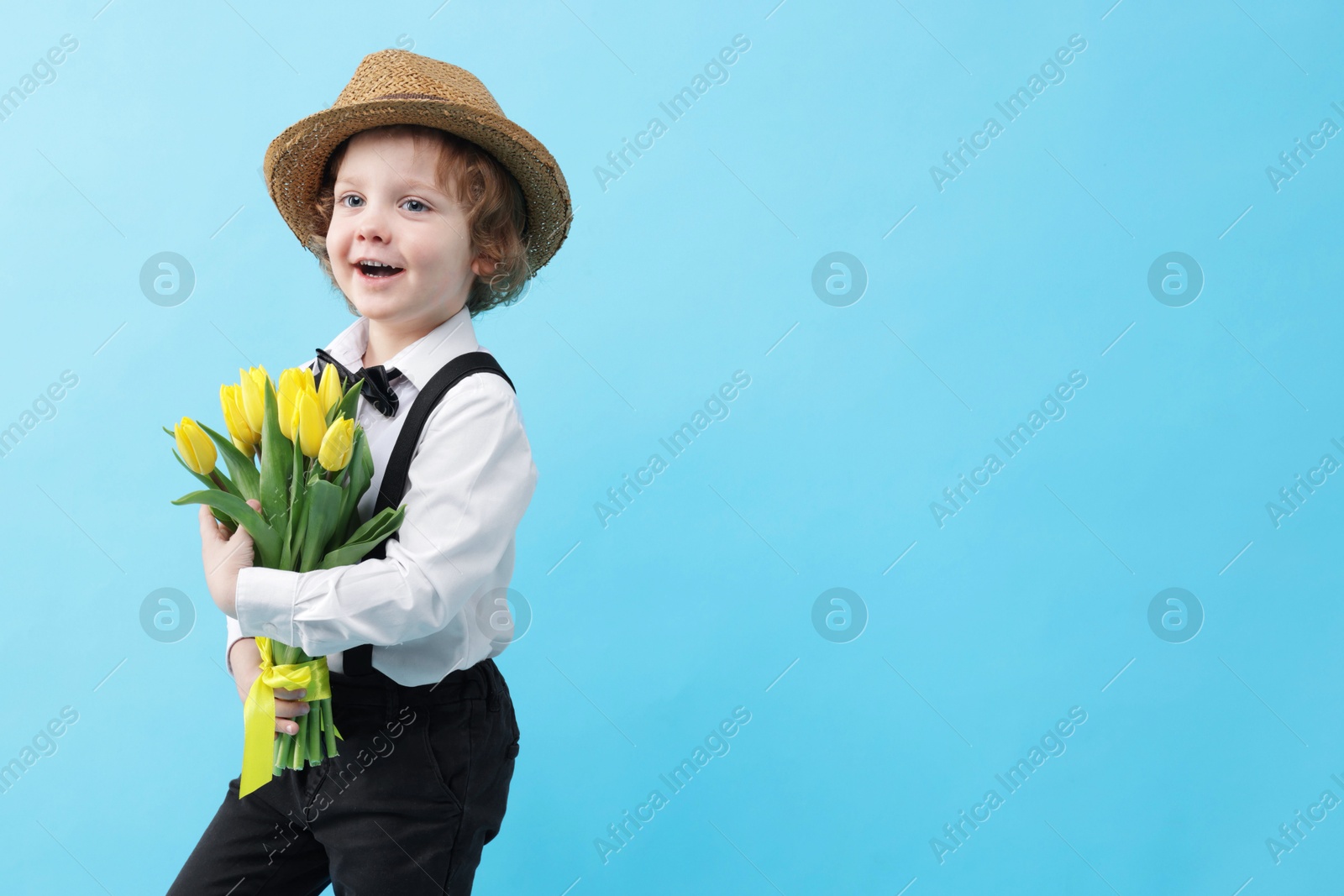 Photo of Cute little boy in wicker hat with bouquet of tulips on light blue background. Space for text