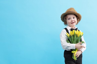 Photo of Cute little boy in wicker hat with bouquet of tulips on light blue background. Space for text