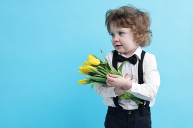 Photo of Cute little boy with bouquet of tulips on light blue background. Space for text