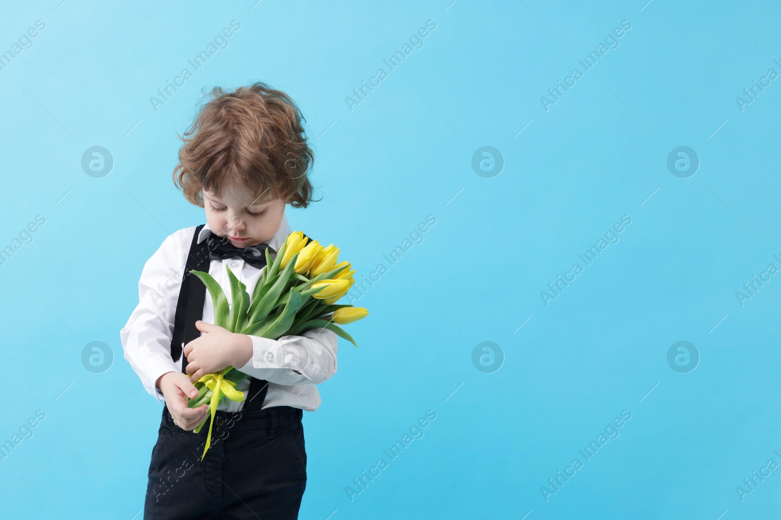 Photo of Cute little boy with bouquet of tulips on light blue background. Space for text