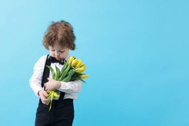 Photo of Cute little boy with bouquet of tulips on light blue background. Space for text